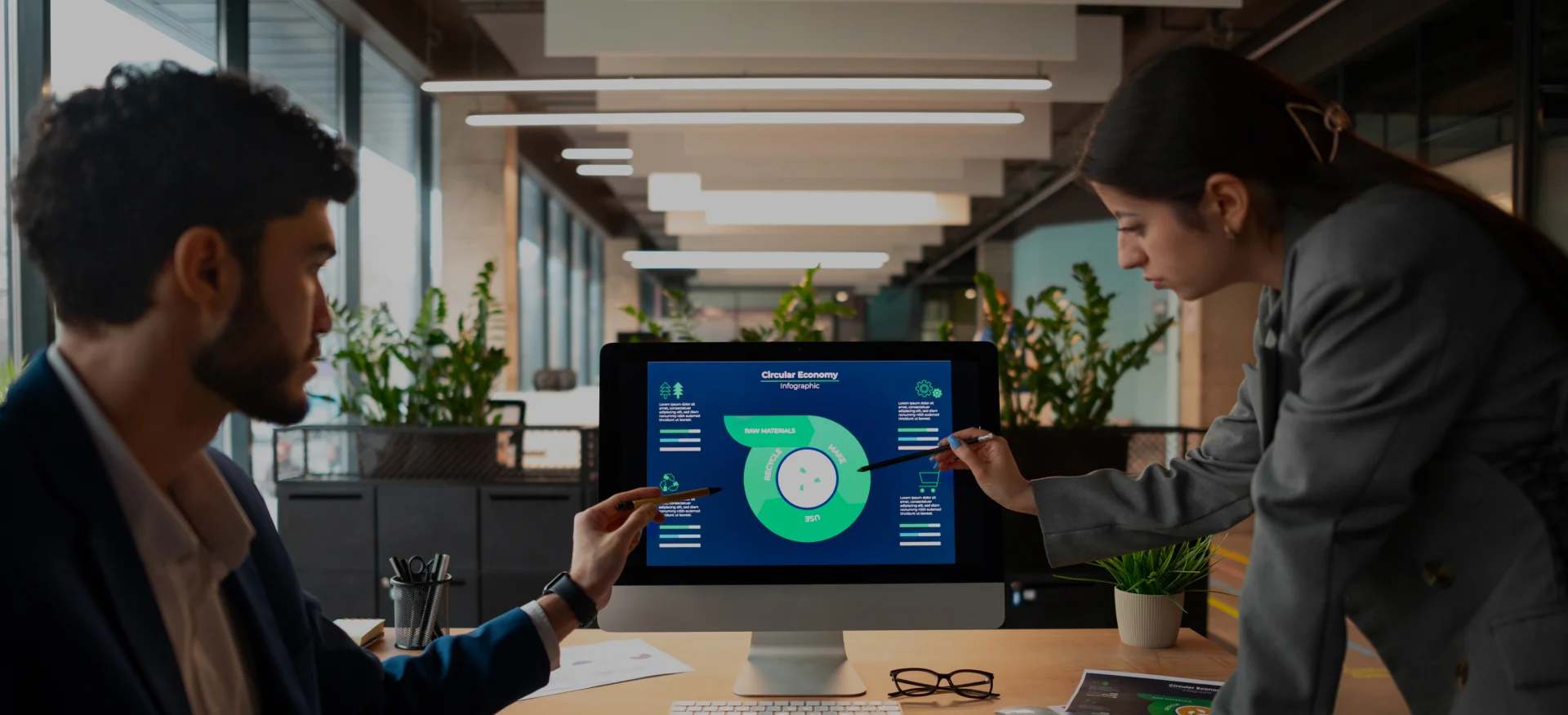 Two professionals discussing data on a computer screen showing a circular diagram in an office setting.