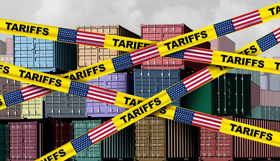Stacked shipping containers blocked by yellow tape labeled "TARIFFS" with U.S. flags.